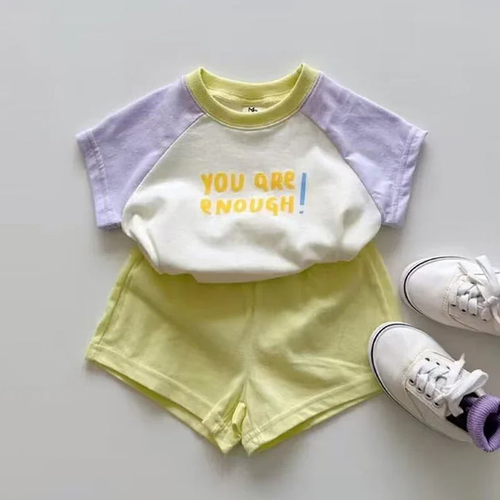 Kids outfit with a white and lavender short-sleeve top saying 'You are enough' paired with yellow shorts and white sneakers