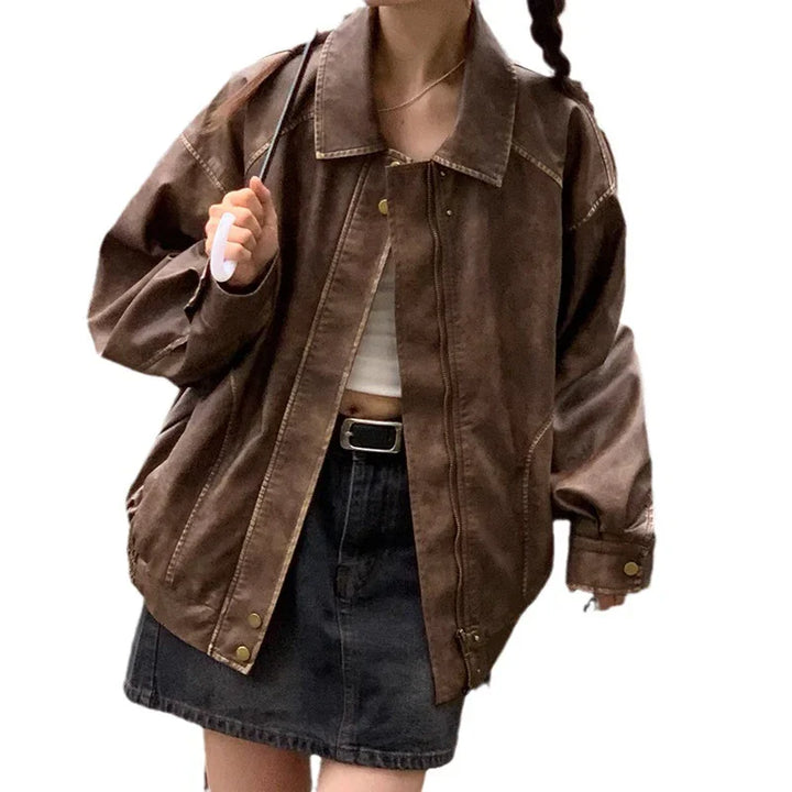 Woman wearing oversized brown leather jacket with black denim skirt and white crop top