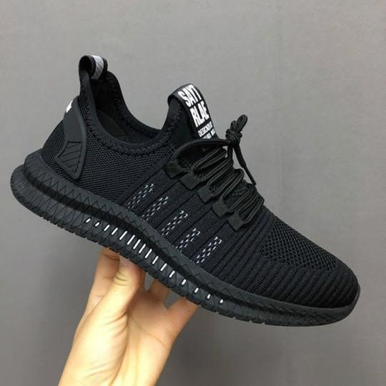 Hand holding modern black knit athletic sneaker with textured sole and lace-up design