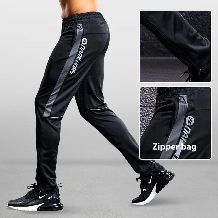 Black athletic pants with dark gray side stripes and zipper pocket detail, worn with black Nike sneakers