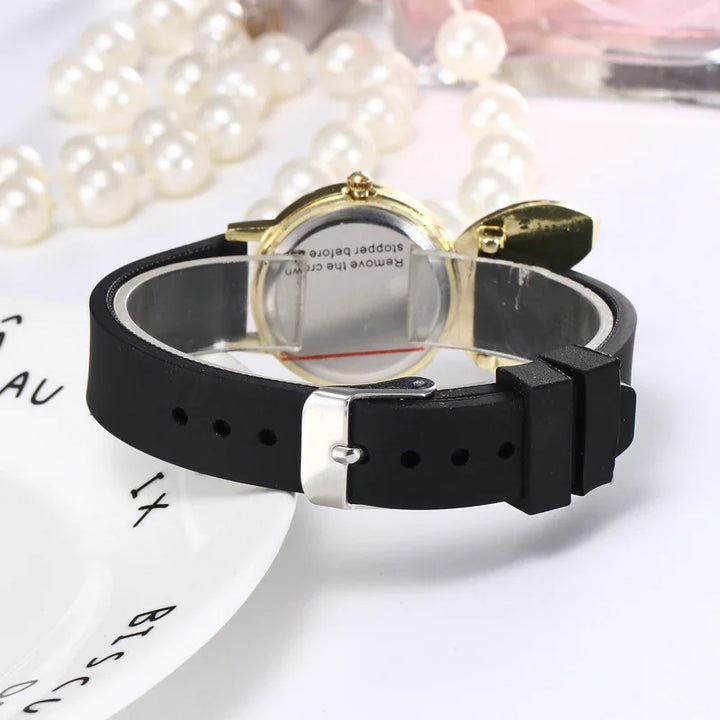 Gold watch with black silicone strap and silver buckle displayed with pearl necklace on white background