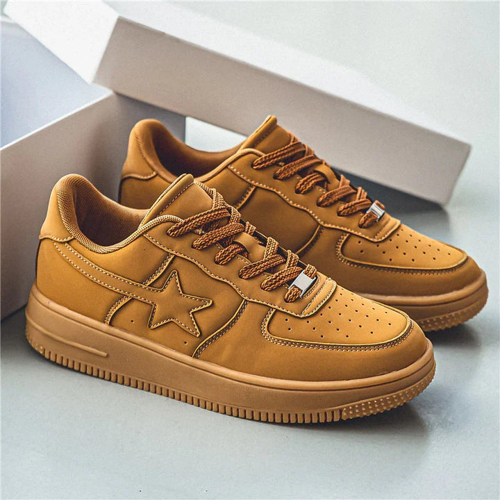 Pair of tan leather sneakers with star design and brown laces on light surface with open shoebox