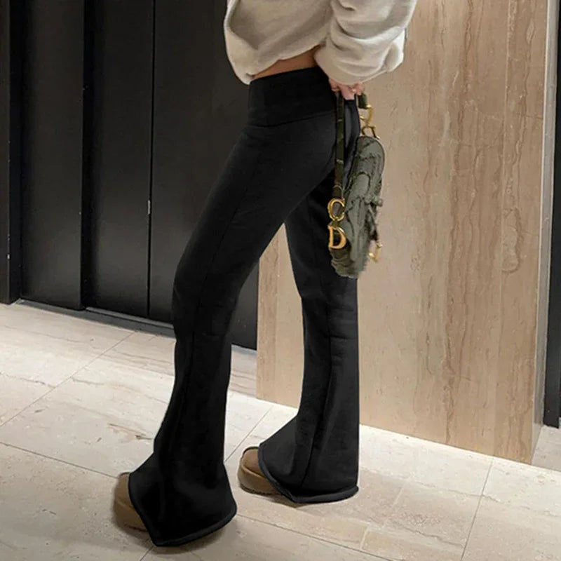 Person wearing black flared pants, beige platform shoes, cream sweater, and holding green designer handbag indoors