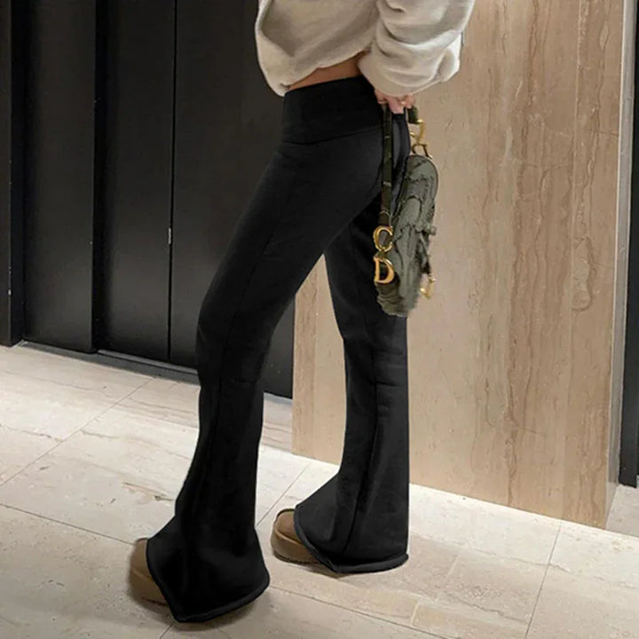 Person wearing black flared pants, beige platform shoes, cream sweater, and holding green designer handbag indoors