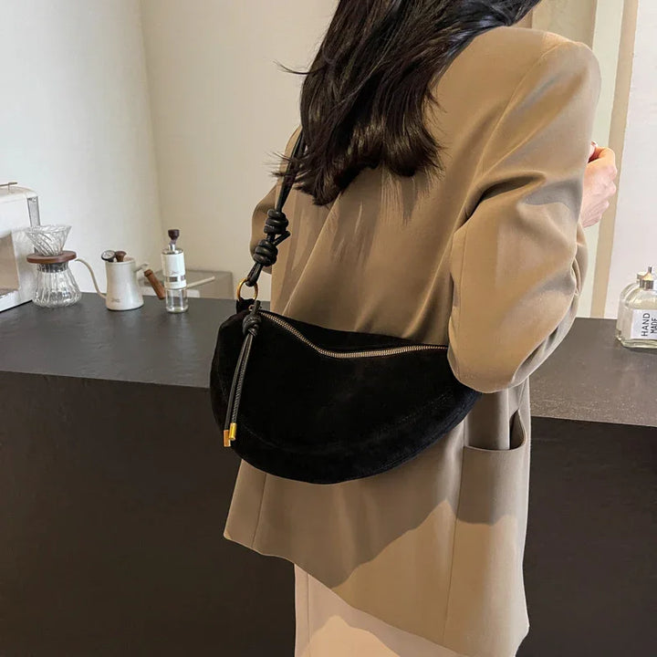 Woman wearing beige blazer with black suede shoulder bag, indoor setting with coffee accessories