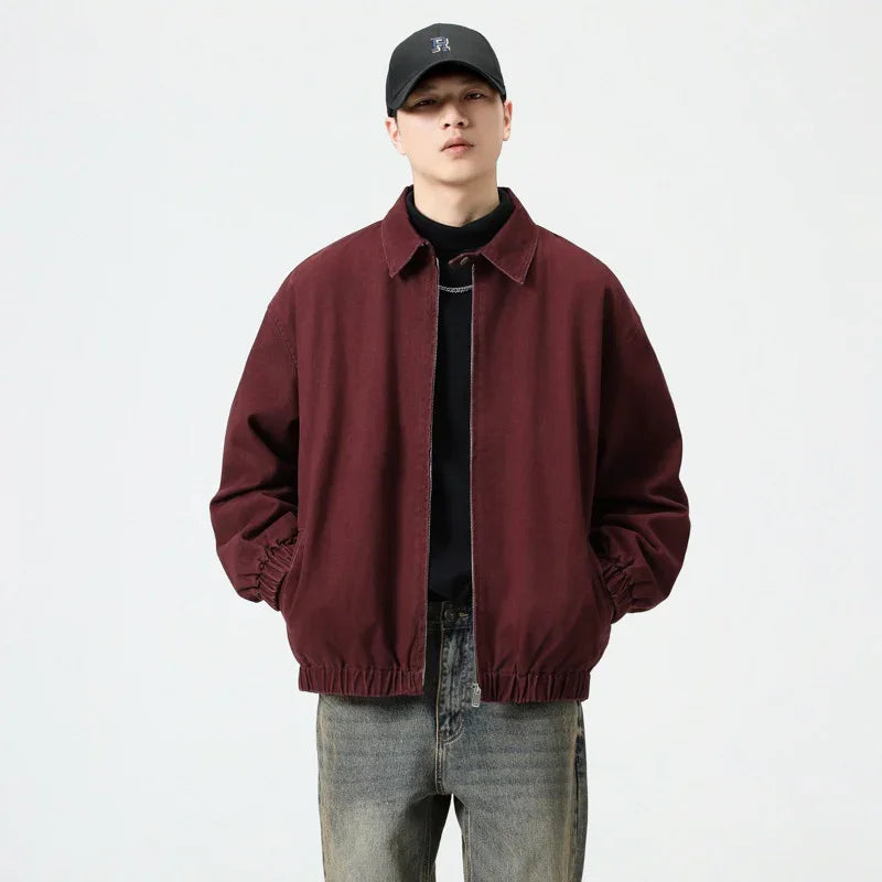 Man wearing maroon casual jacket with elastic cuffs, gray jeans, black shirt, and black cap