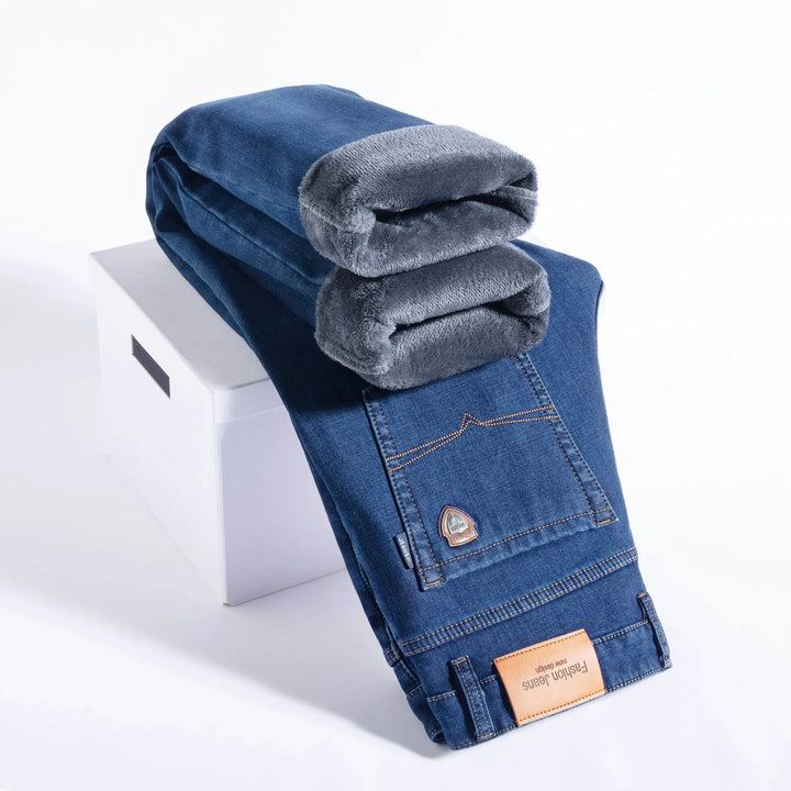 Folded blue denim jeans with gray fleece lining resting on white box, fashion label visible