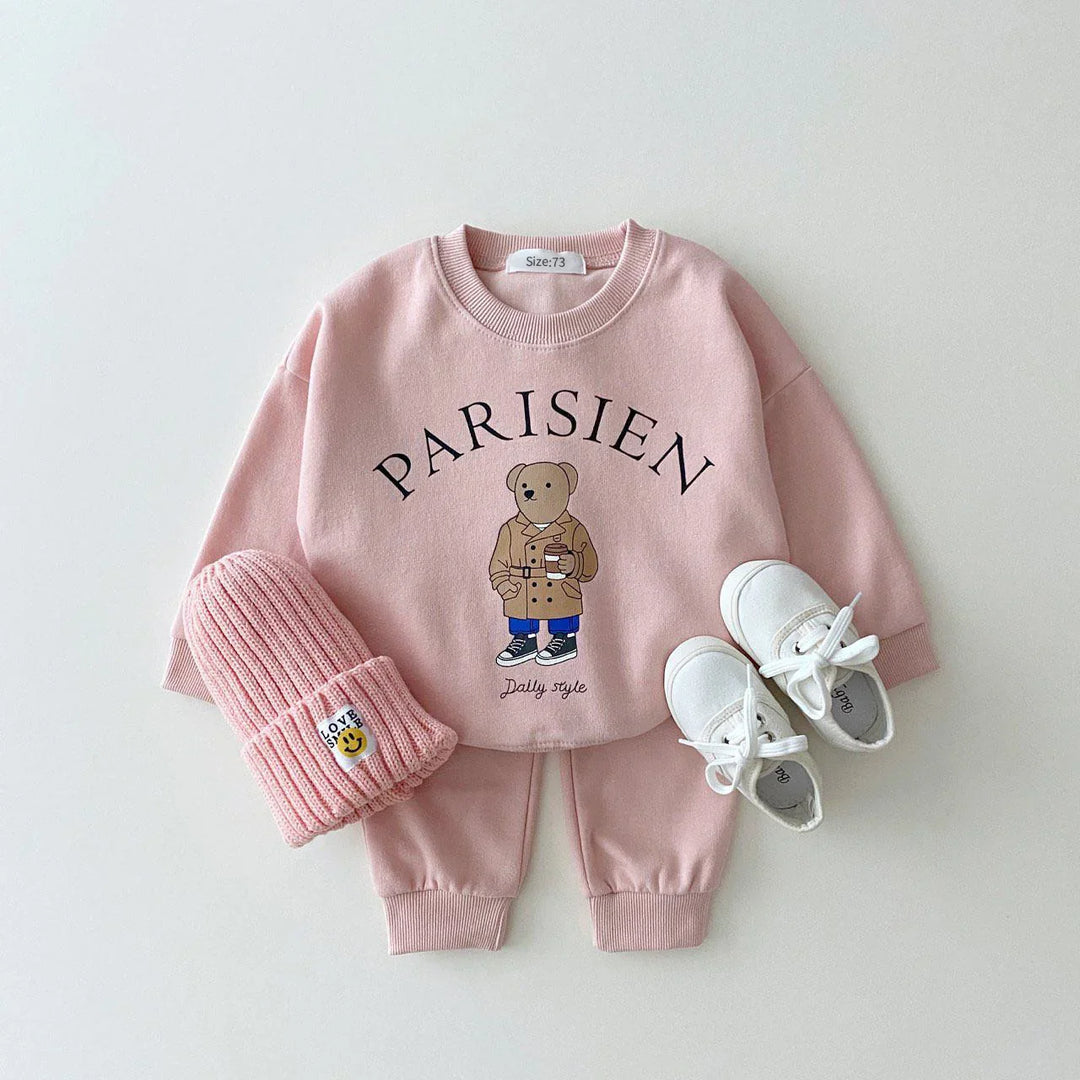 Pink toddler outfit with bear print sweatshirt saying Parisien, matching pants, pink knit hat, and white shoes