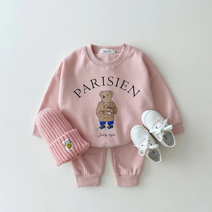 Pink toddler outfit with bear print sweatshirt saying Parisien, matching pants, pink knit hat, and white shoes