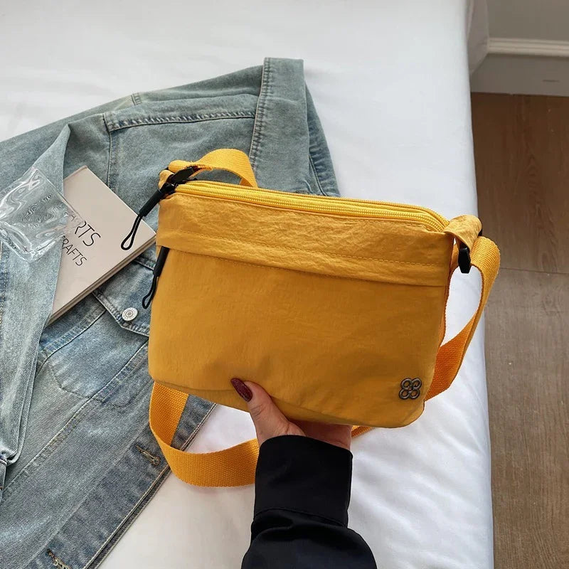 Hand holding a small mustard yellow crossbody bag over denim jacket on white bed