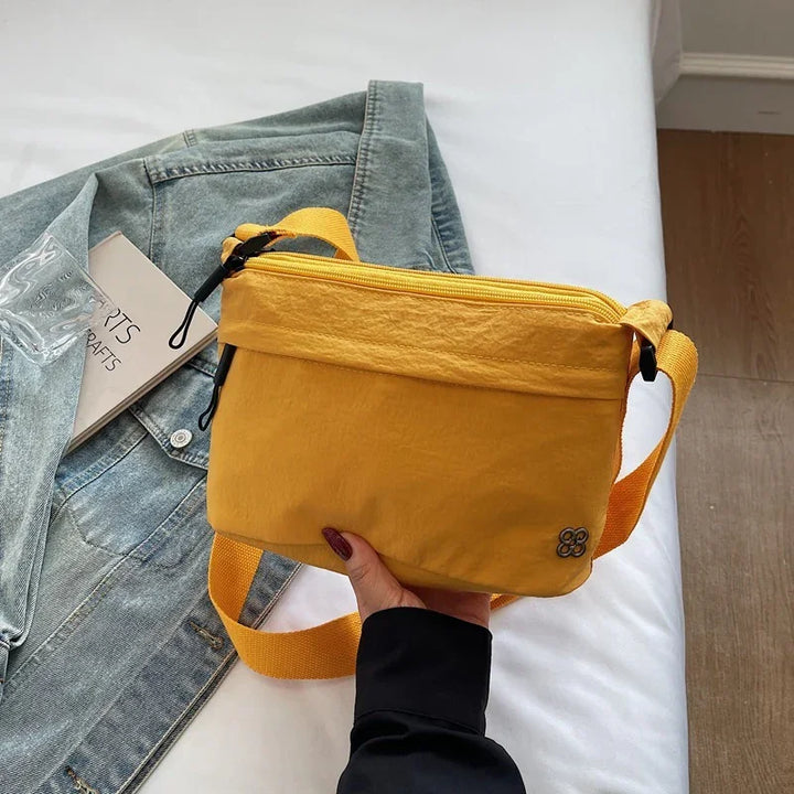 Hand holding a small mustard yellow crossbody bag over denim jacket on white bed