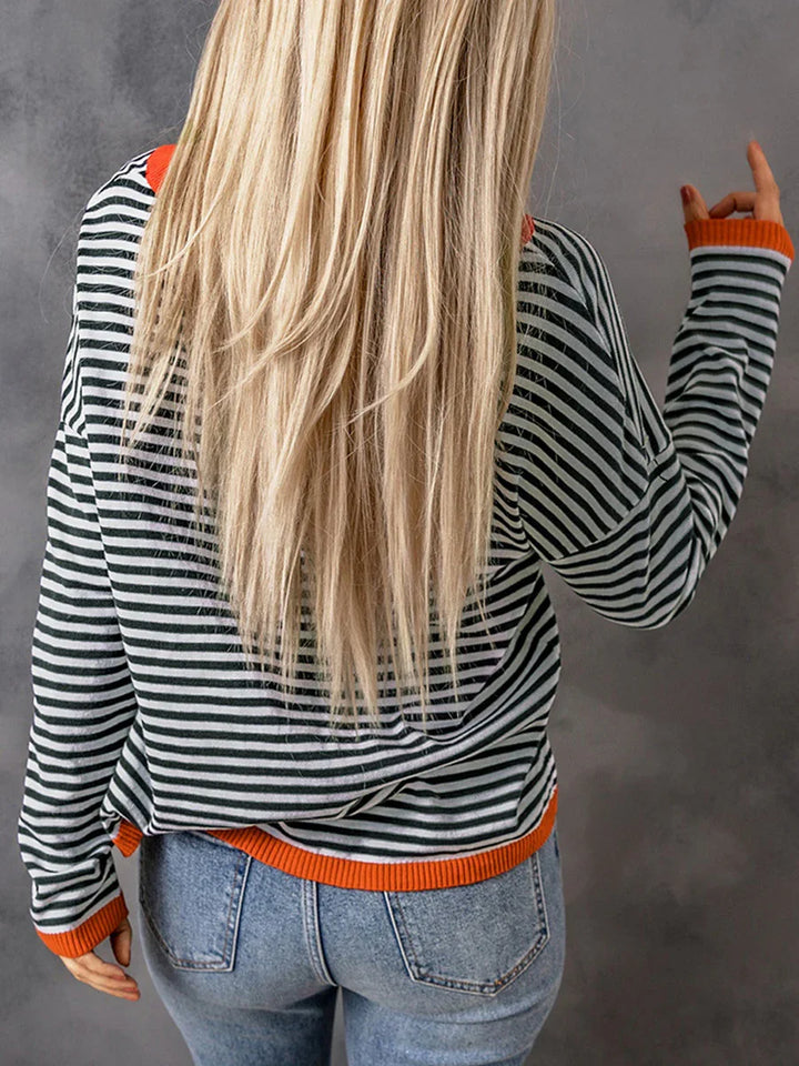 Back view of woman with long blonde hair wearing black and white striped sweater with orange trim and blue jeans