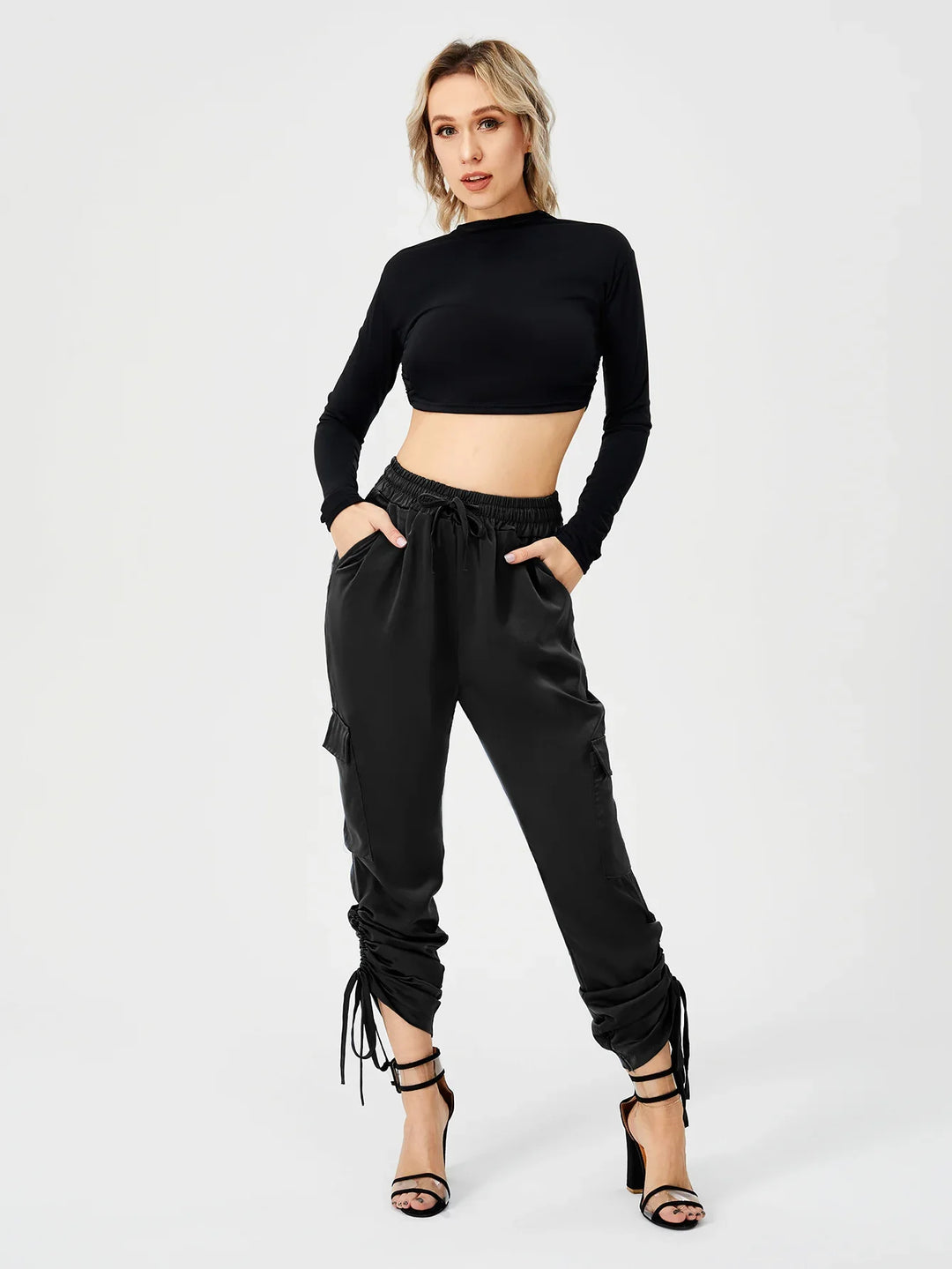 Woman wearing black long sleeve crop top and ruched satin jogger pants with black strappy heels