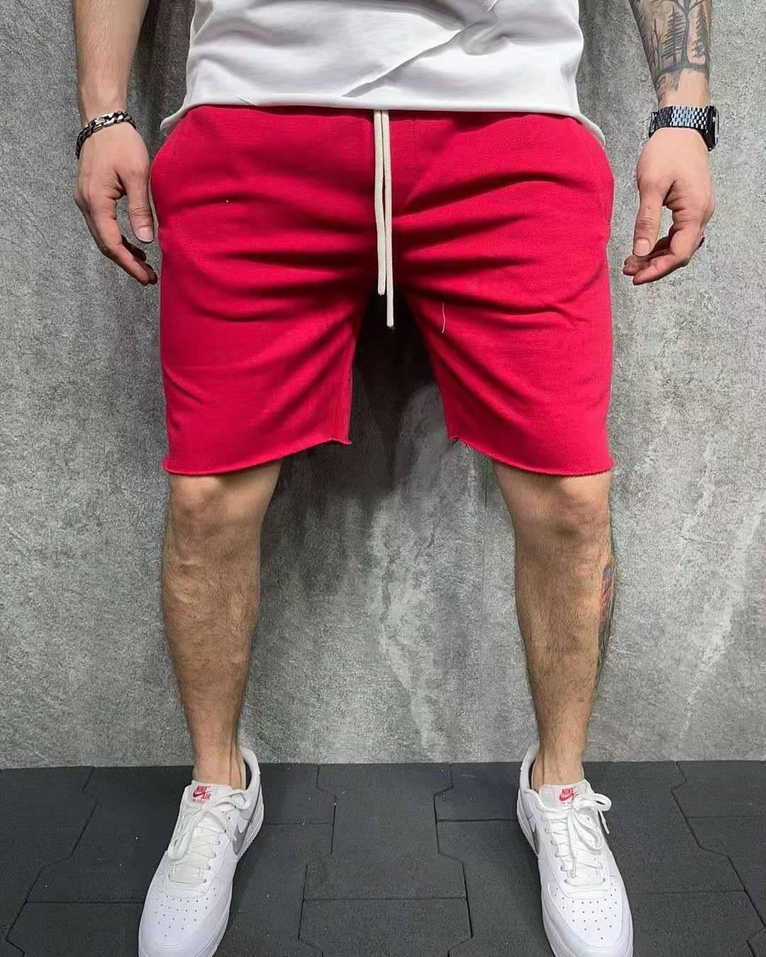 Man wearing red drawstring shorts and white Nike sneakers standing on black tiles with gray textured wall background