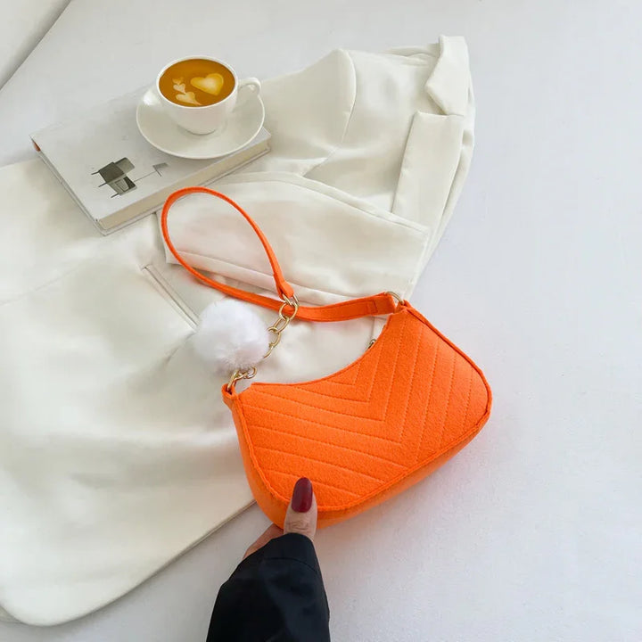 Orange quilted handbag with white pompom on white blazer and cup of coffee with latte art
