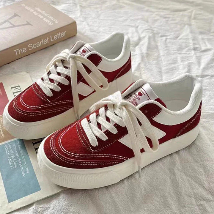 Pair of red and white low-top canvas sneakers with white laces on bed next to a book