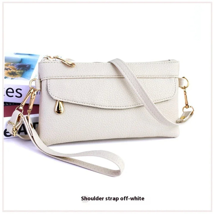 Off-white textured leather wristlet with shoulder strap and gold zipper accents on white background