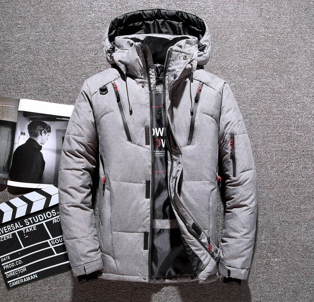 Gray padded winter jacket with hood and black zipper details laid on carpet with open magazine and clapperboard