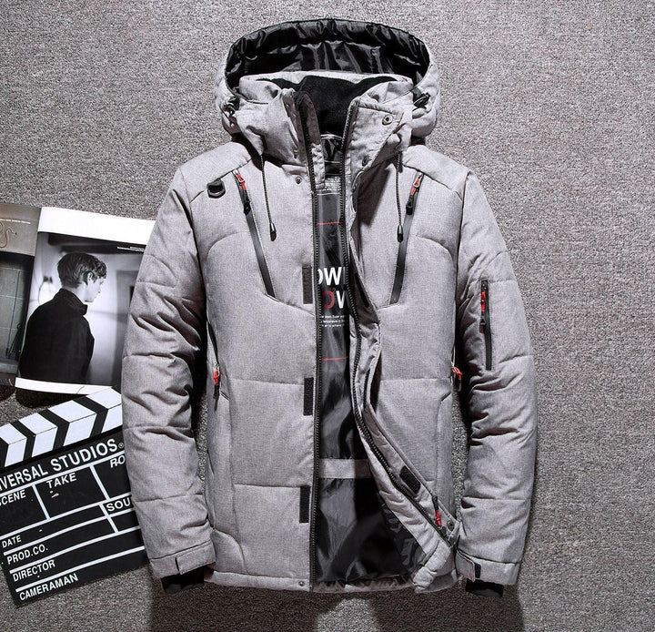 Gray padded winter jacket with hood and black zipper details laid on carpet with open magazine and clapperboard