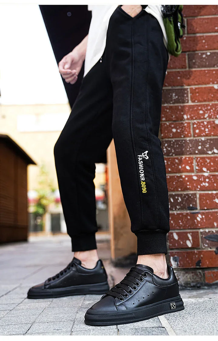 Close-up of black casual jogger pants with 'FashionR 8090' logo and black sneakers on urban street