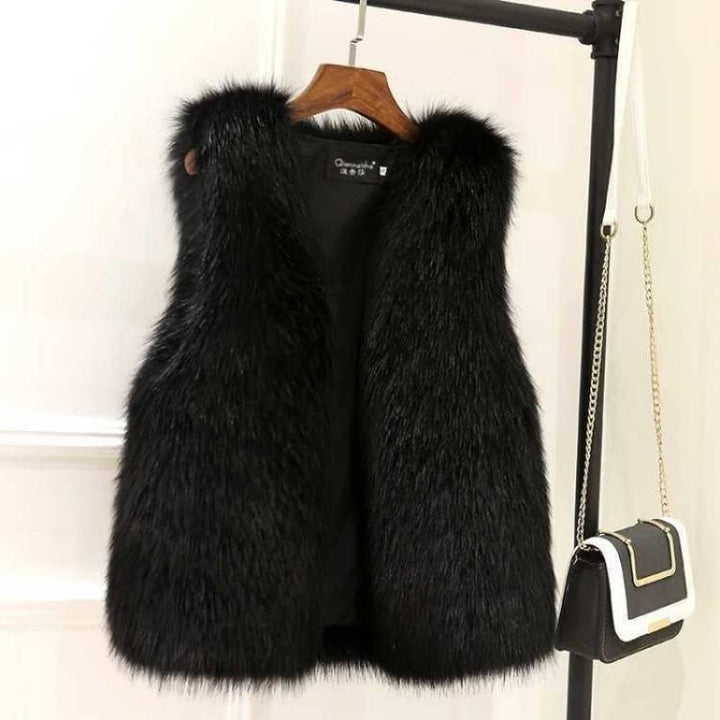 Black faux fur sleeveless vest hanging on wooden hanger next to small black and white crossbody purse