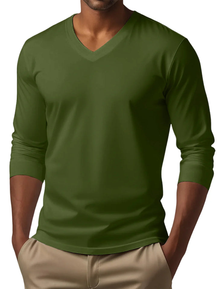 Man wearing olive green long sleeve V-neck shirt with beige pants, hands in pockets