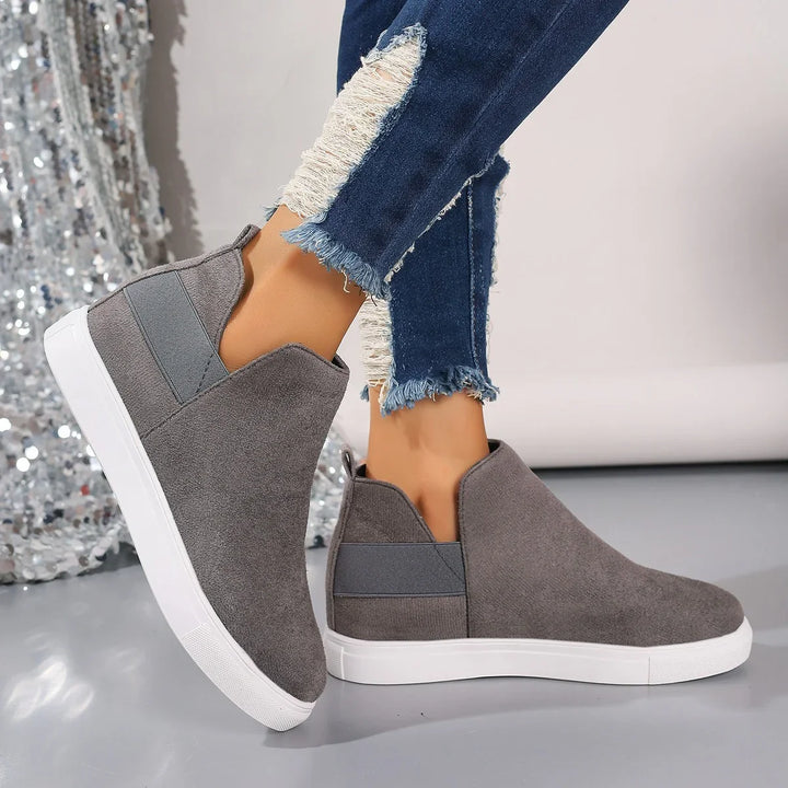 Grey suede slip-on sneakers with white sole worn with blue distressed jeans on reflective floor