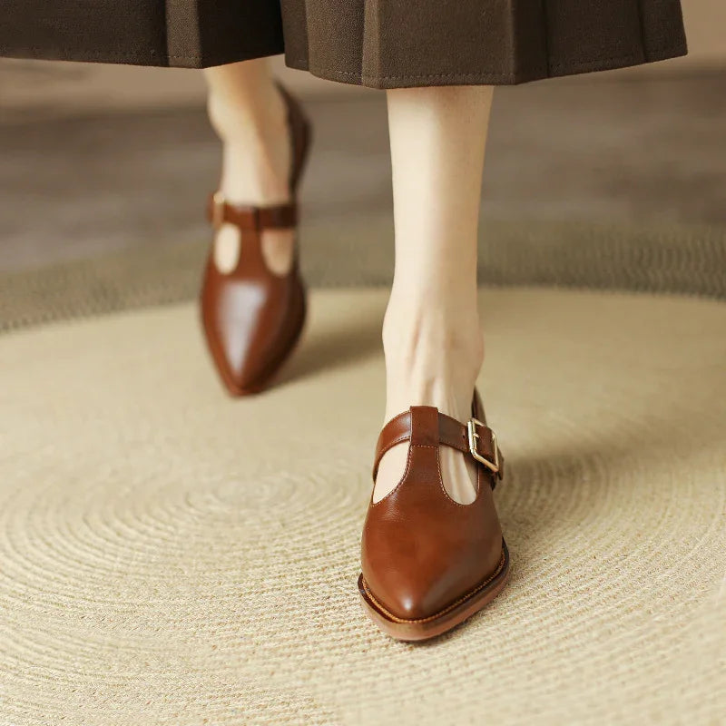 Close-up of brown leather T-strap buckle shoes worn with brown wide-leg pants on beige woven rug