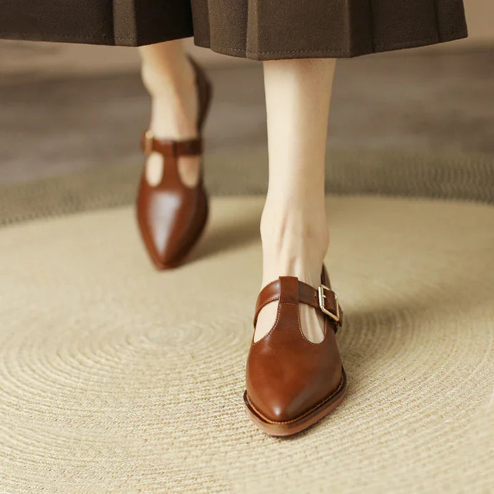 Close-up of brown leather T-strap buckle shoes worn with brown wide-leg pants on beige woven rug