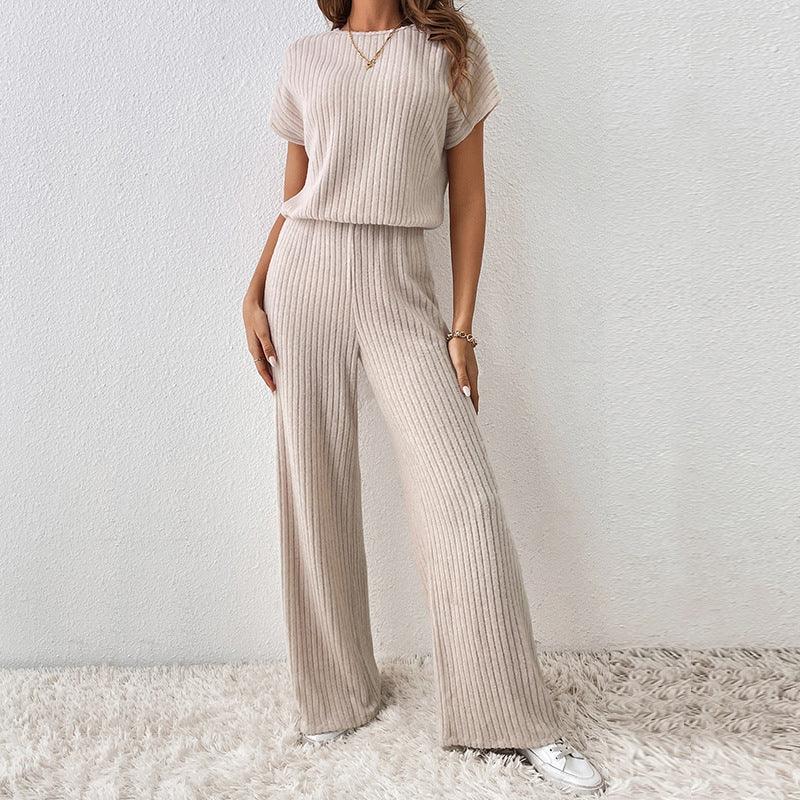 Woman wearing beige ribbed knit short sleeve top and wide leg pants set with white sneakers on fluffy rug