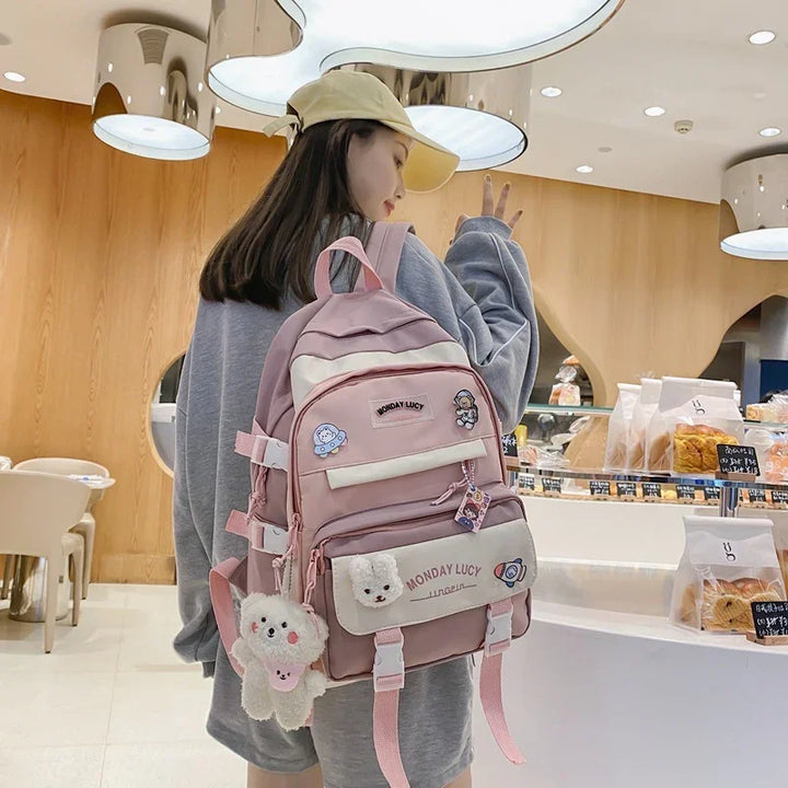 Woman in grey sweatshirt and yellow cap carrying pink Monday Lucy backpack with plush charms in bakery