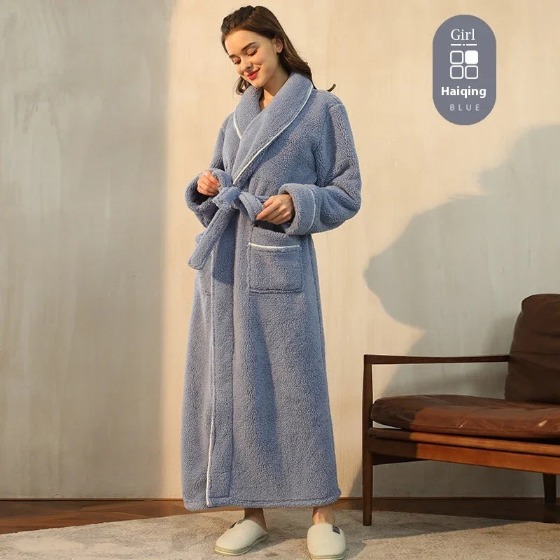 Woman wearing long blue fleece bathrobe with belt standing indoors near wooden chair