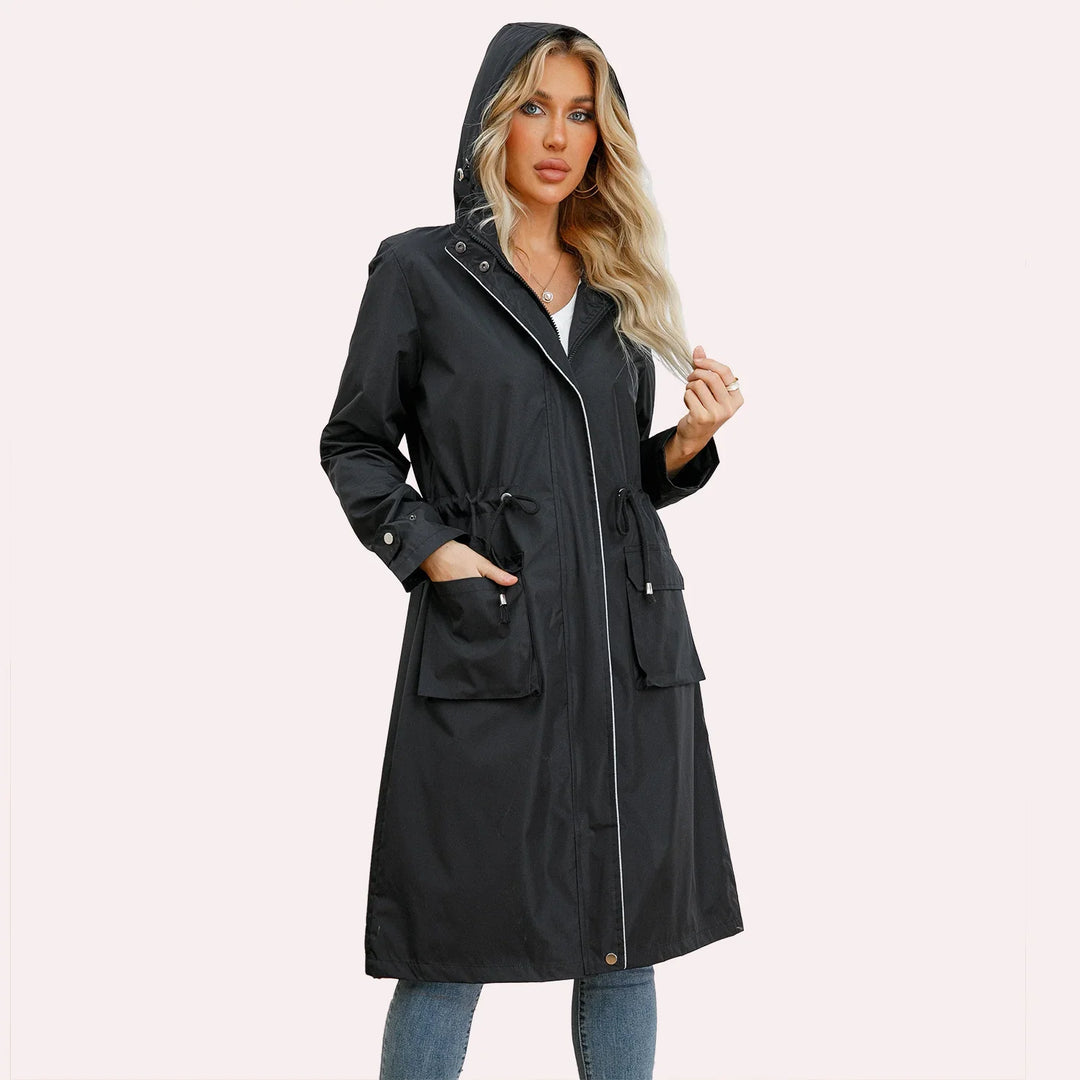 Woman wearing black hooded long raincoat with front pockets and silver snaps, styled with jeans