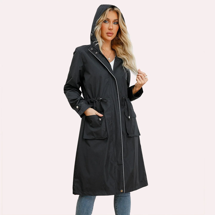 Woman wearing black hooded long raincoat with front pockets and silver snaps, styled with jeans