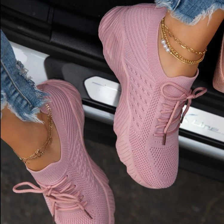 Close-up of pink knit sneakers worn with ripped jeans and gold ankle bracelets