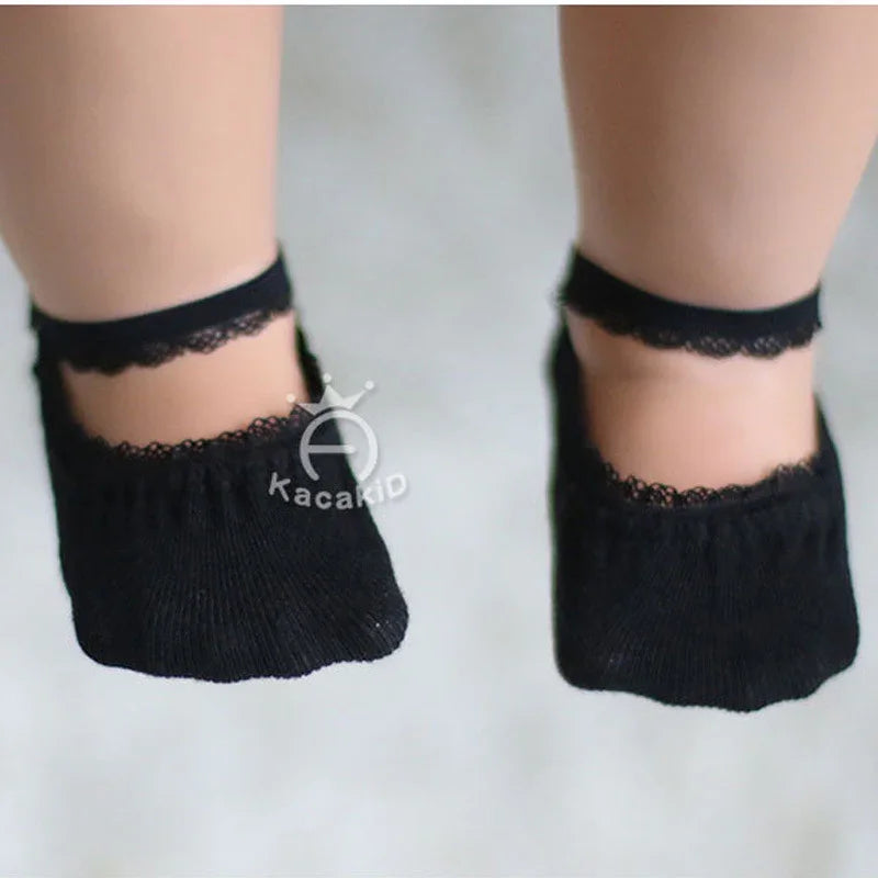 Baby feet wearing black lace-trimmed ankle socks on a light background
