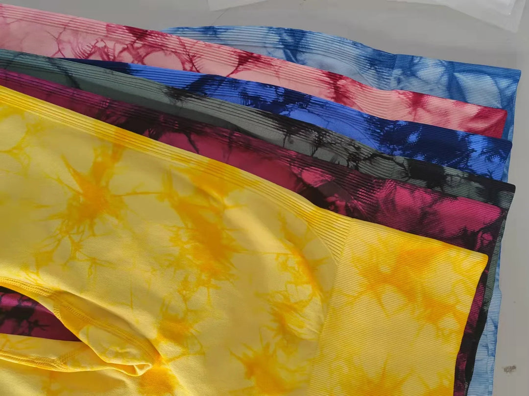 Stack of colorful tie-dye leggings in yellow, pink, black, and blue with ribbed texture