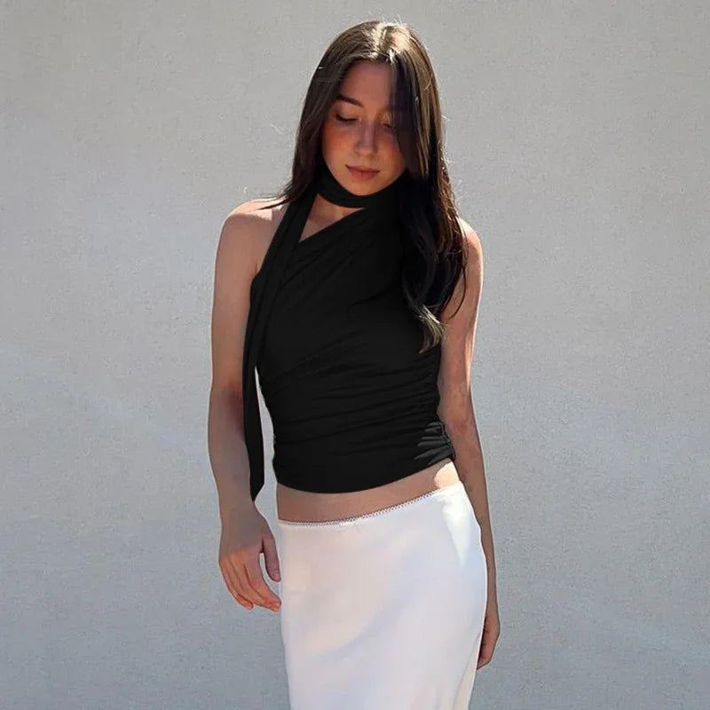 Woman with long dark hair wearing black halter top and white skirt against plain wall