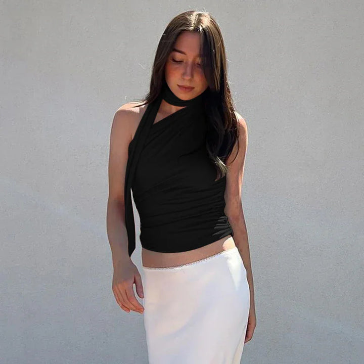 Woman with long dark hair wearing black halter top and white skirt against plain wall