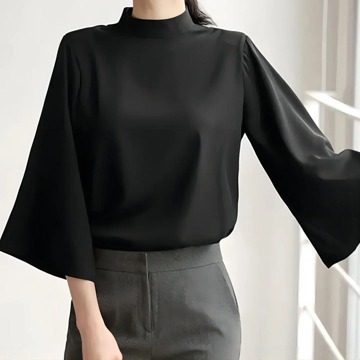 Woman wearing black high-neck blouse with wide bell sleeves and gray high-waisted pants
