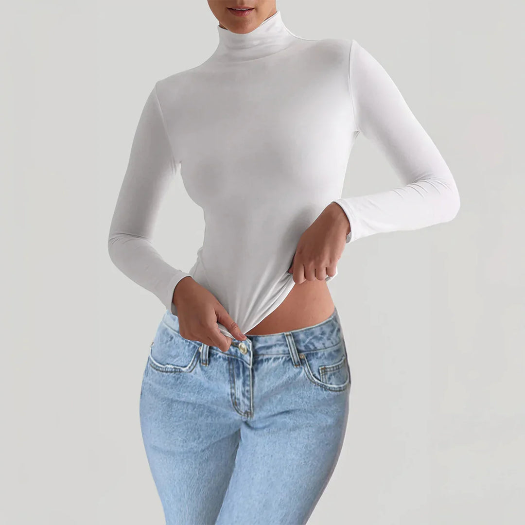 Woman wearing a white long-sleeve turtleneck top paired with light blue high-waisted jeans against a neutral background