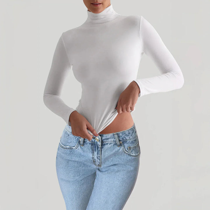 Woman wearing a white long-sleeve turtleneck top paired with light blue high-waisted jeans against a neutral background