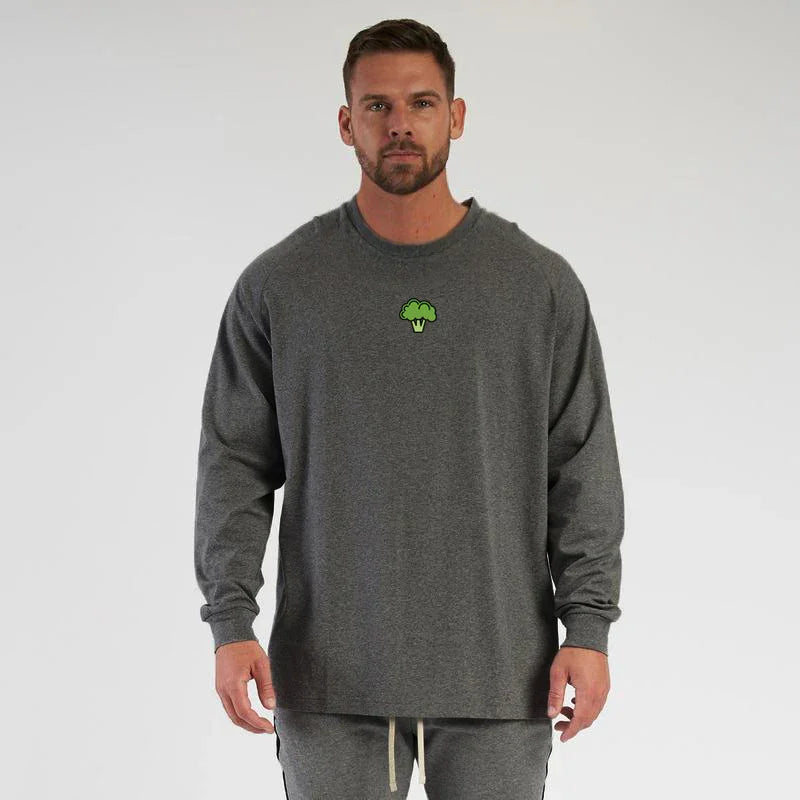 Man wearing dark gray long sleeve shirt with small green broccoli logo on chest