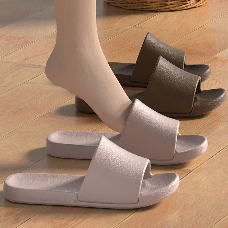Foot wearing light beige open-toe slides next to brown slides on wooden floor