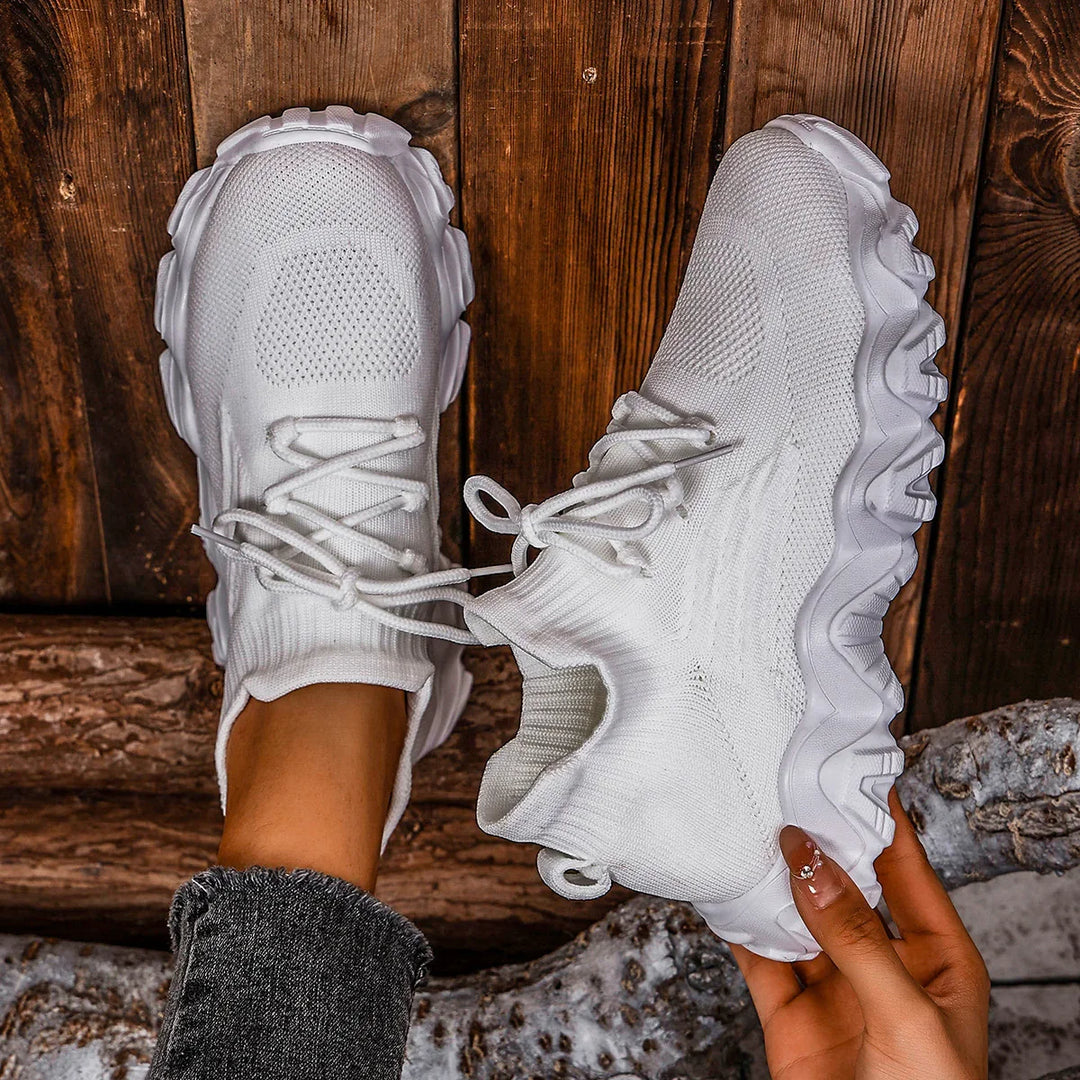 White knit sock sneakers with thick textured soles on wooden floor, styled with black denim jeans