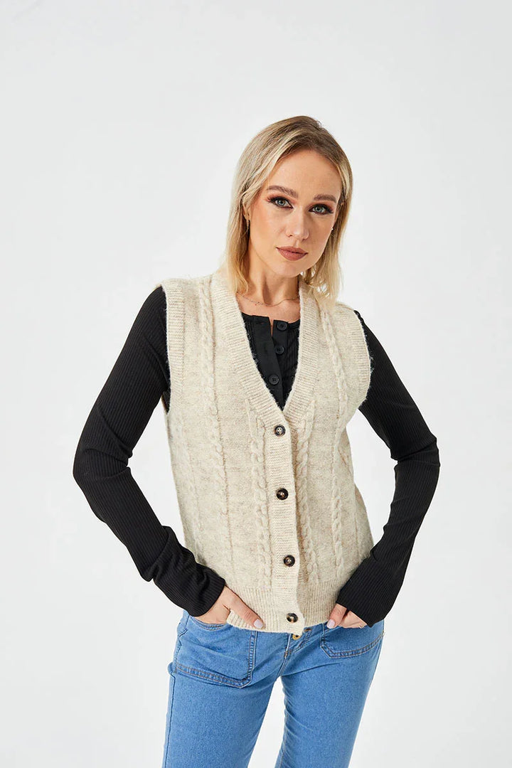 Blonde woman wearing cream cable knit buttoned vest over black long sleeve top and blue jeans