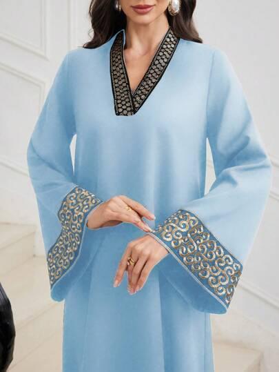 Woman wearing light blue dress with embellished black and gold V-neckline and wide cuff sleeves