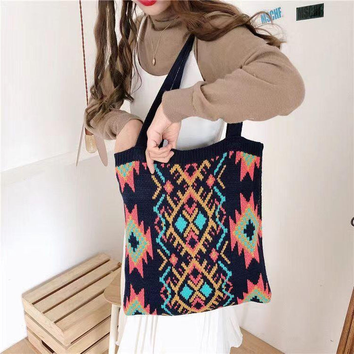 Woman holding black tote bag with colorful geometric tribal pattern over white dress and brown sweater