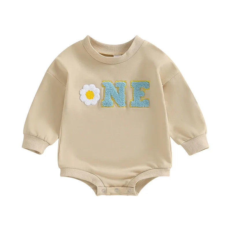 Beige baby romper with long sleeves and snap buttons, featuring blue ONE lettering and a white daisy applique