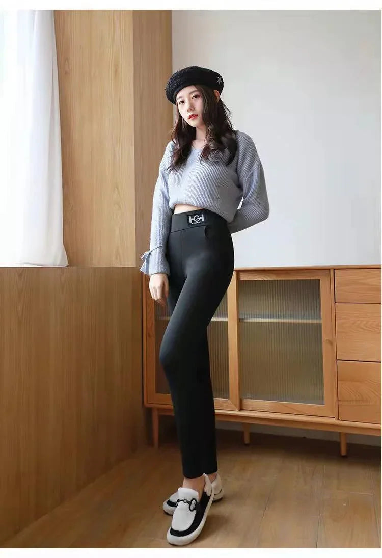 Young woman wearing cropped gray sweater, black leggings, black beret, and white loafers indoors